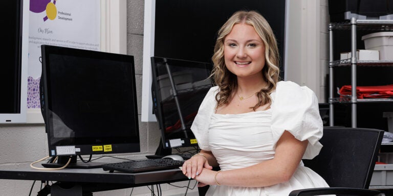Leah Carr sits at a desk with a computer monitor