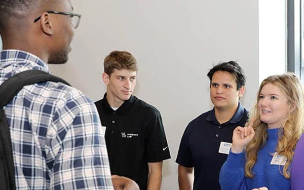 An ECU student standing with his back to the camera, talks to other students attending the ECU Pharma Fest.