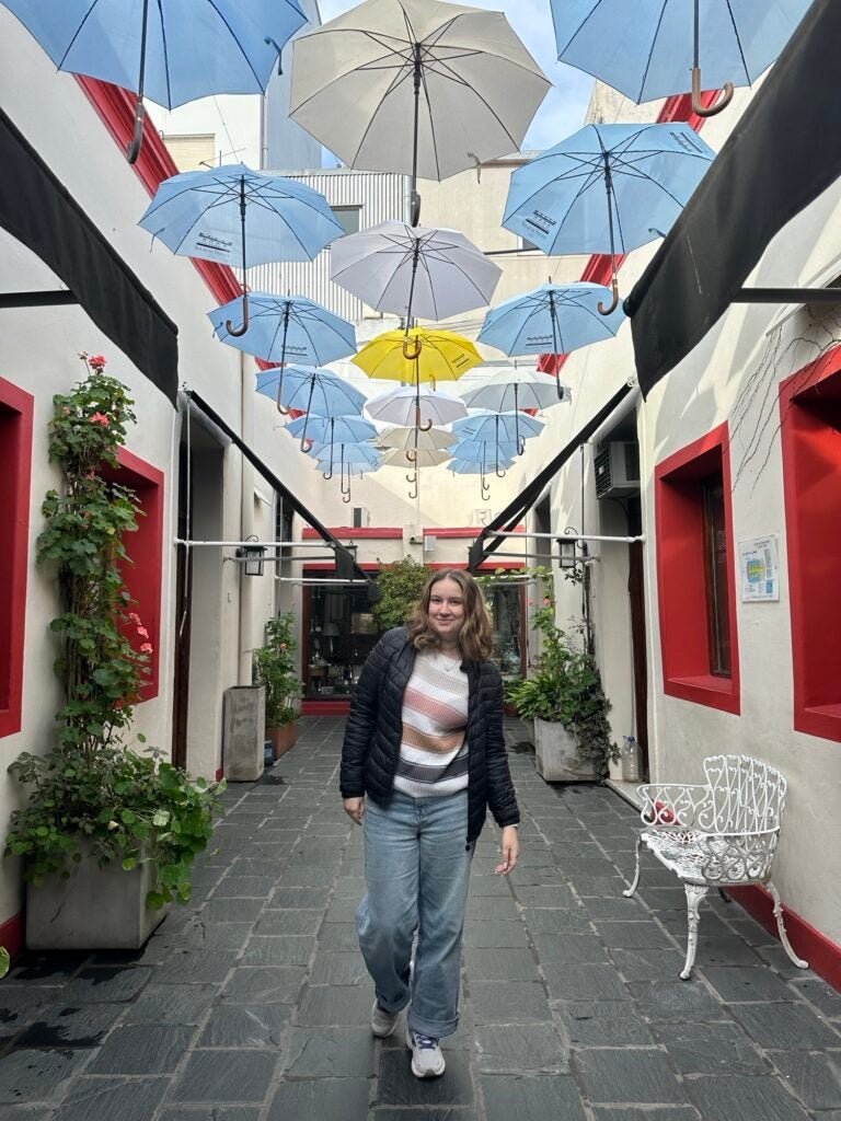 ECU student Mikaela Trank walks between two buildings with Japanese paper umbrellas hanging above and between the buildings.