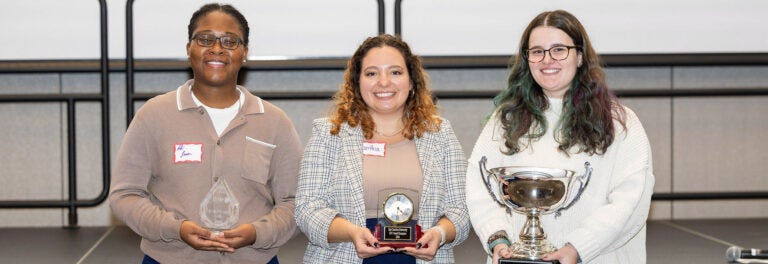 Three women stand holding trophies in the Main Campus Student Center ballroom.