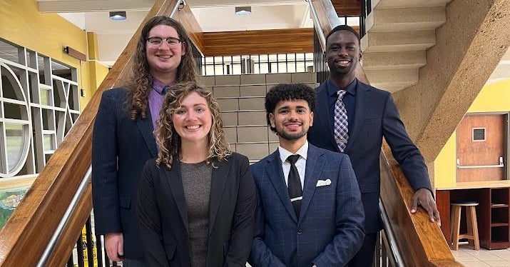 Four East Carolina University graduate students in business attire stand on a set of stairs at a conference.