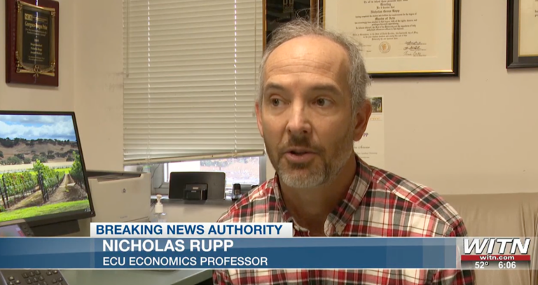 A man with receding gray hair is seen in his office through a digital interview produced by a local news station.