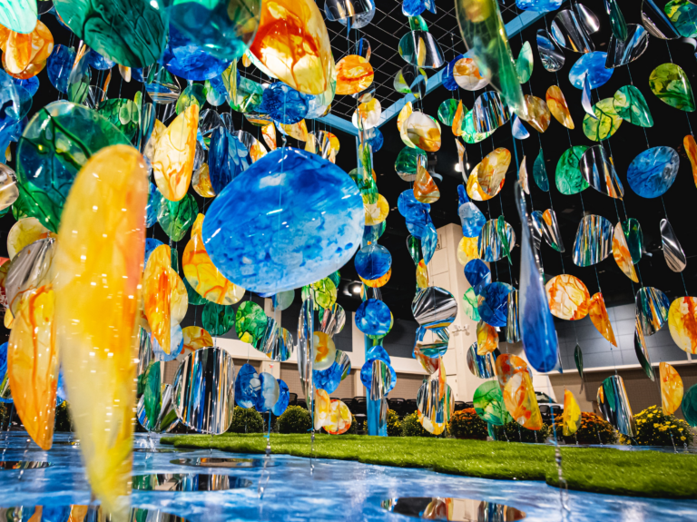 A collection of colorful blown glass art hanging over a blue pond.