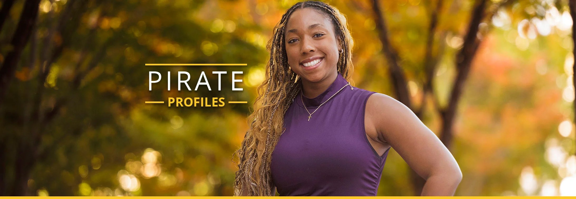 A woman in a purple tank top and long hair stands with her hand on her hip. The background contains trees with yellow, gold, and green fall-colored leaves.