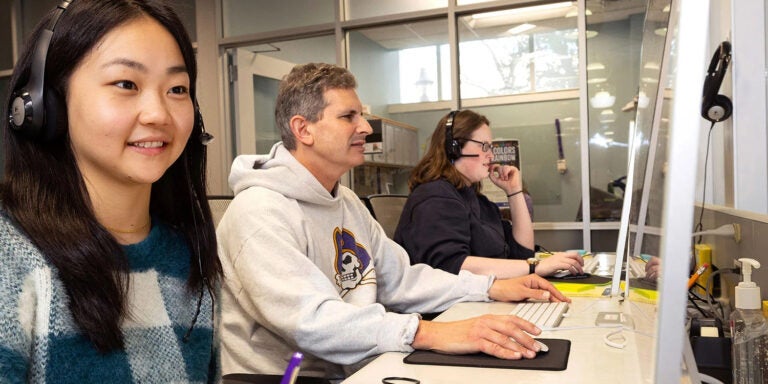 Student workers in the university Writing Center sit in front of a long table while working at computers.