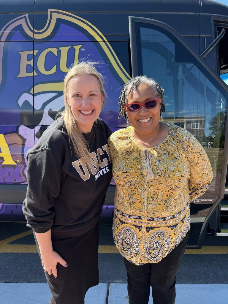  Joanne Hersey, in a black University of North Carolina Pembroke sweater, stands with April Reed, in a flowy yellow blouse, in front of the ECU Pirates bus during a tour of the University of North Carolina Pembroke campus.