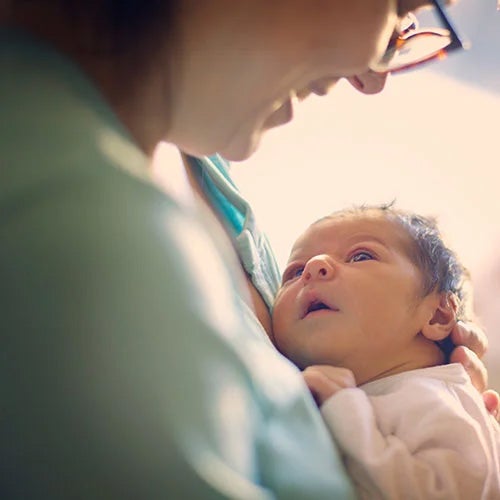 A women holds a newborn baby which is looking up at the woman's face.