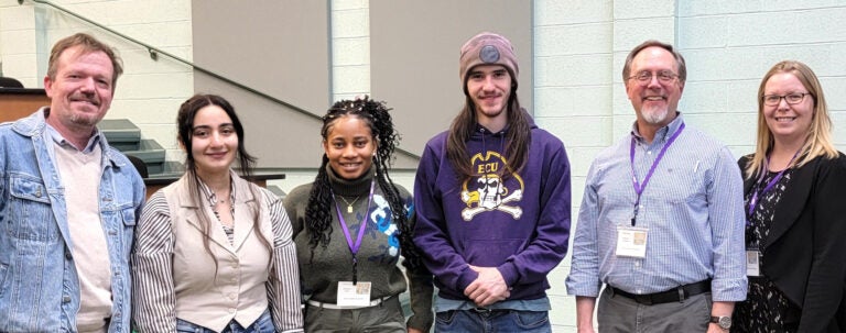 Students and faculty stand in a group in a conference room