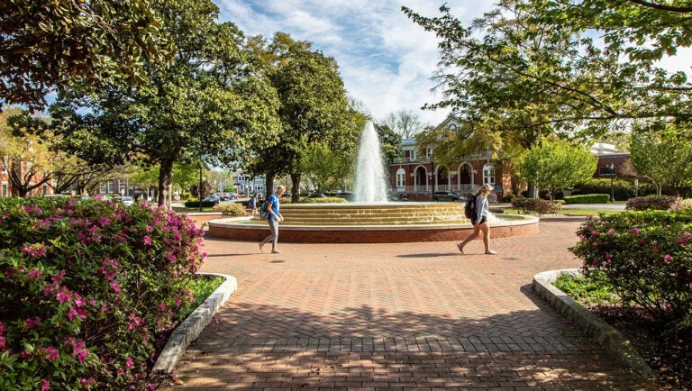 Two students walk by the fountain on Wright Plaza with trees and flowers in bloom.