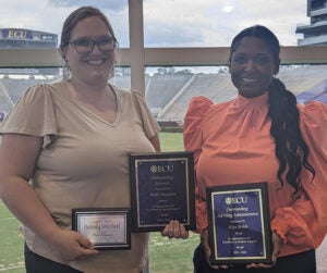 Beth and Kiya hold their awards with a view of the Pirates football stadium in the background