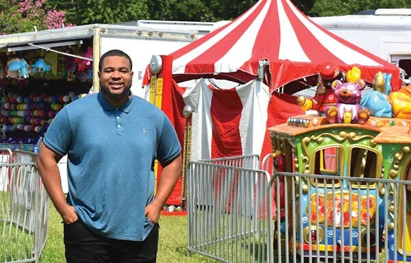 Man standing outside with a carnival tent and fence in the background