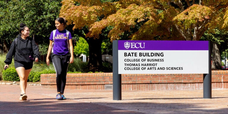 ECU students Lauren Aponte and Lynoshka Padilla walk on campus. The Bate Building and sign is to the right of the image.