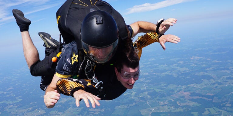 Two people in mid-free fall during a tandem skydive with the sky and earth in the background